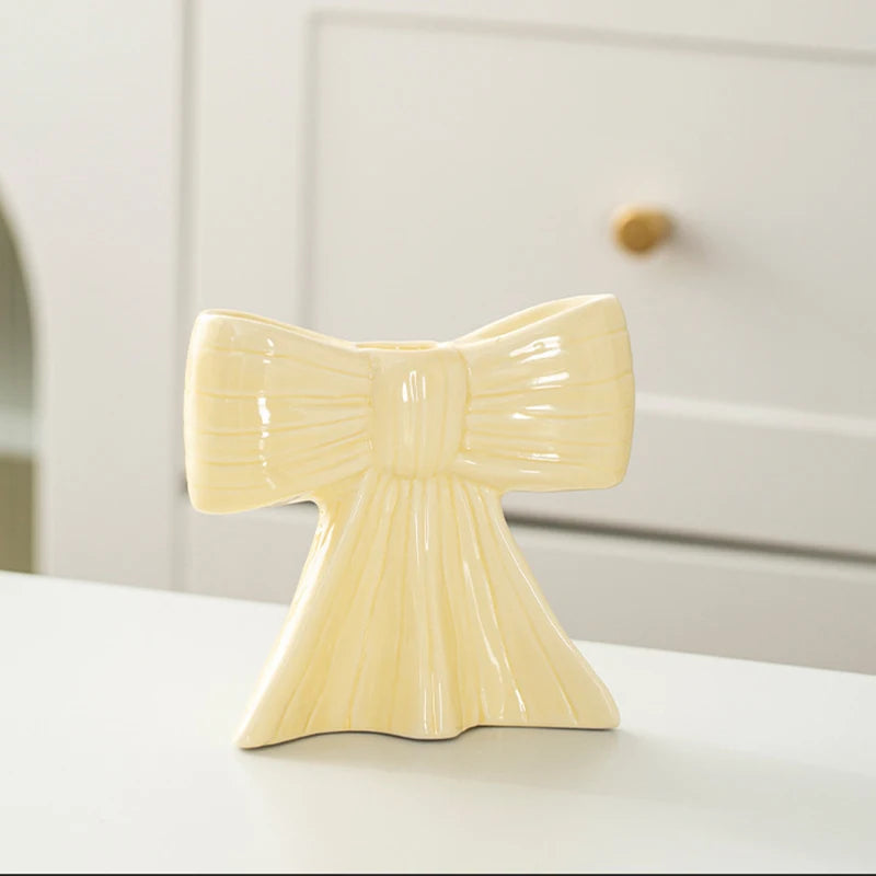 A pale yellow ceramic bow candle holder with vertical ribbed texture sitting on a white surface.