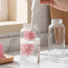 A hand is using a white bottle brush to clean baby bottles stored in glass jars.