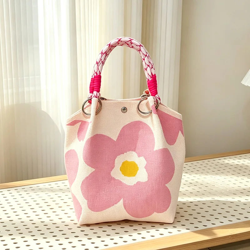A pink floral jacquard knitted shoulder bag with white and yellow accents displayed on a wooden surface.