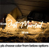 A glowing neon sign spelling Just Married is displayed on a fluffy gold rug next to a book.