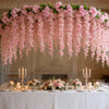 A pink silk wisteria hanging vine garland draped over a long table decorated with flowers and candles.