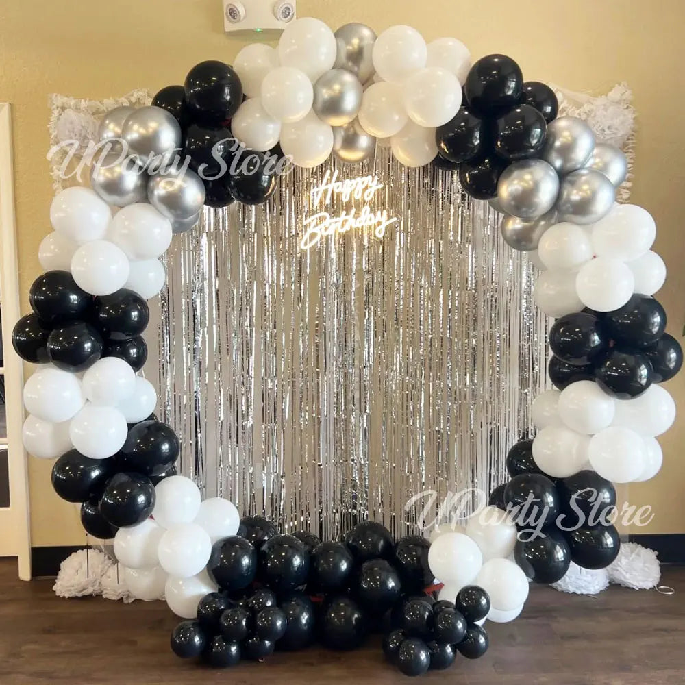 A circular party backdrop decorated with white and black balloons framed by metallic silver fringe curtains.