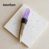A purple amethyst crystal point set in a wooden scepter wand displayed on a white square card.