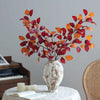 An autumn beech simulation flower branch decoration in shades of red, orange, and maroon displayed in a white vase.