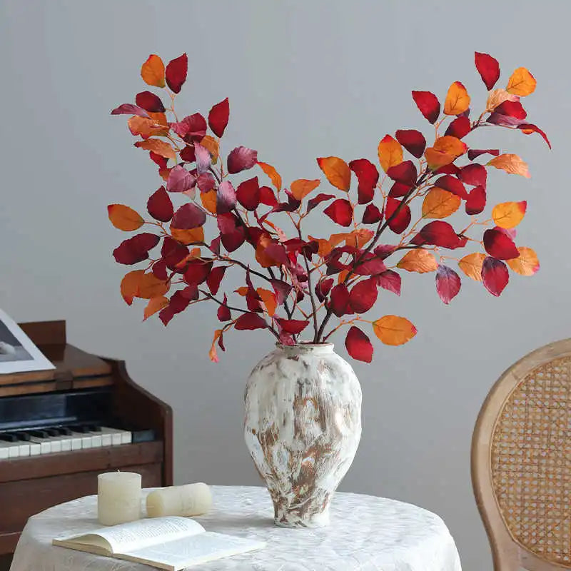 An autumn beech simulation flower branch decoration in shades of red, orange, and maroon displayed in a white vase.
