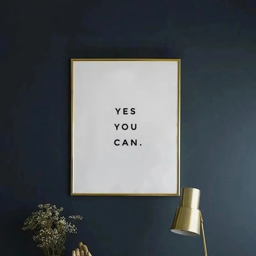 A framed canvas art print with the text YES YOU CAN on a white background mounted on a dark blue wall.