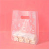 A clear plastic gift bag with a white daisy print design filled with small white treats on a pink background.