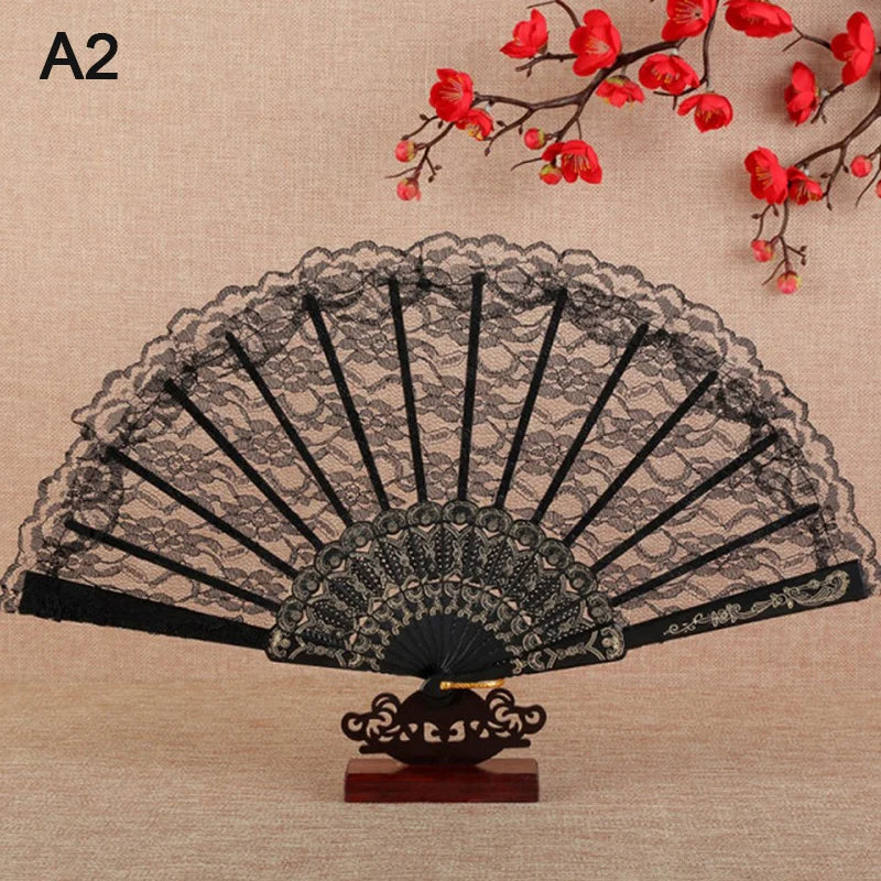 Elegant black lace folding hand fan with red floral accents displayed on a wooden stand.