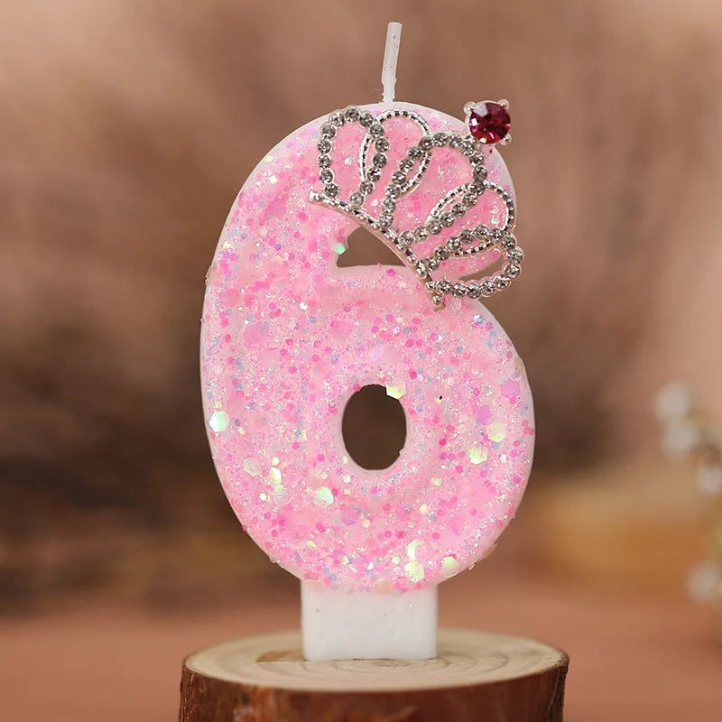 Pink glitter number six birthday candle with a silver crown detail on a wooden base