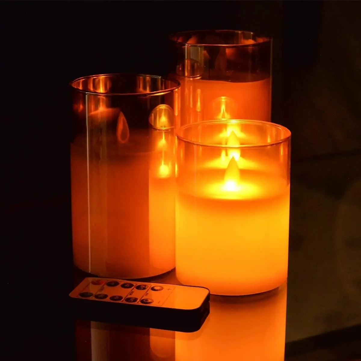 Three glass pillar candles glowing warmly in a dark setting, with a remote timer visible.