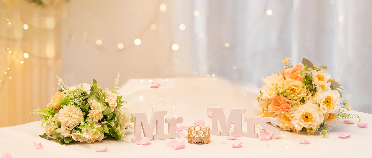 A bridal centerpiece featuring a bouquet of yellow and peach roses and pink petals on a white table.