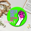 A bright green button pin featuring the text GREEN DAY PRESENTS American Mint and a hand with a pink heart design.