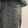 A close-up of a denim pant leg featuring a layered silver chain belt with small star charms.