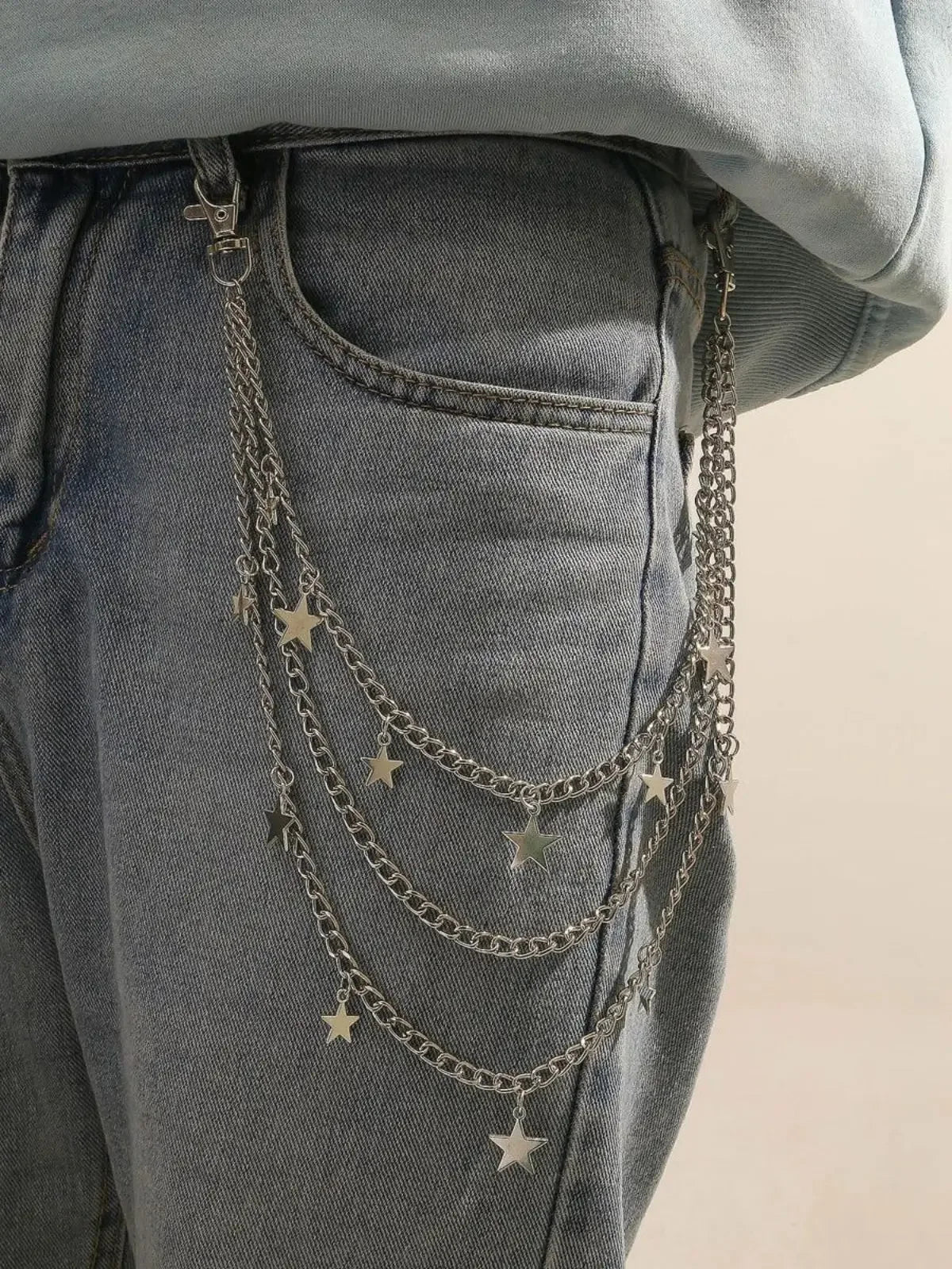 A close-up of a denim pant leg featuring a layered silver chain belt with small star charms.