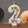 A white birthday candle shaped like the number 2 decorated with colorful candy beads