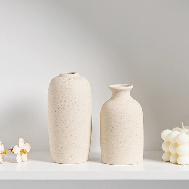 Two minimalist ceramic vases in a light beige tone displayed on a white shelf.