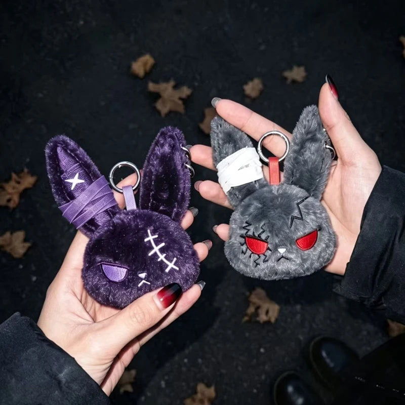A hand holds a dark purple velvet bunny plush keychain with silver rings against a dark background.