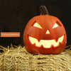 Linterna de calabaza de cerámica naranja con cara amenazadora, sobre paja.
