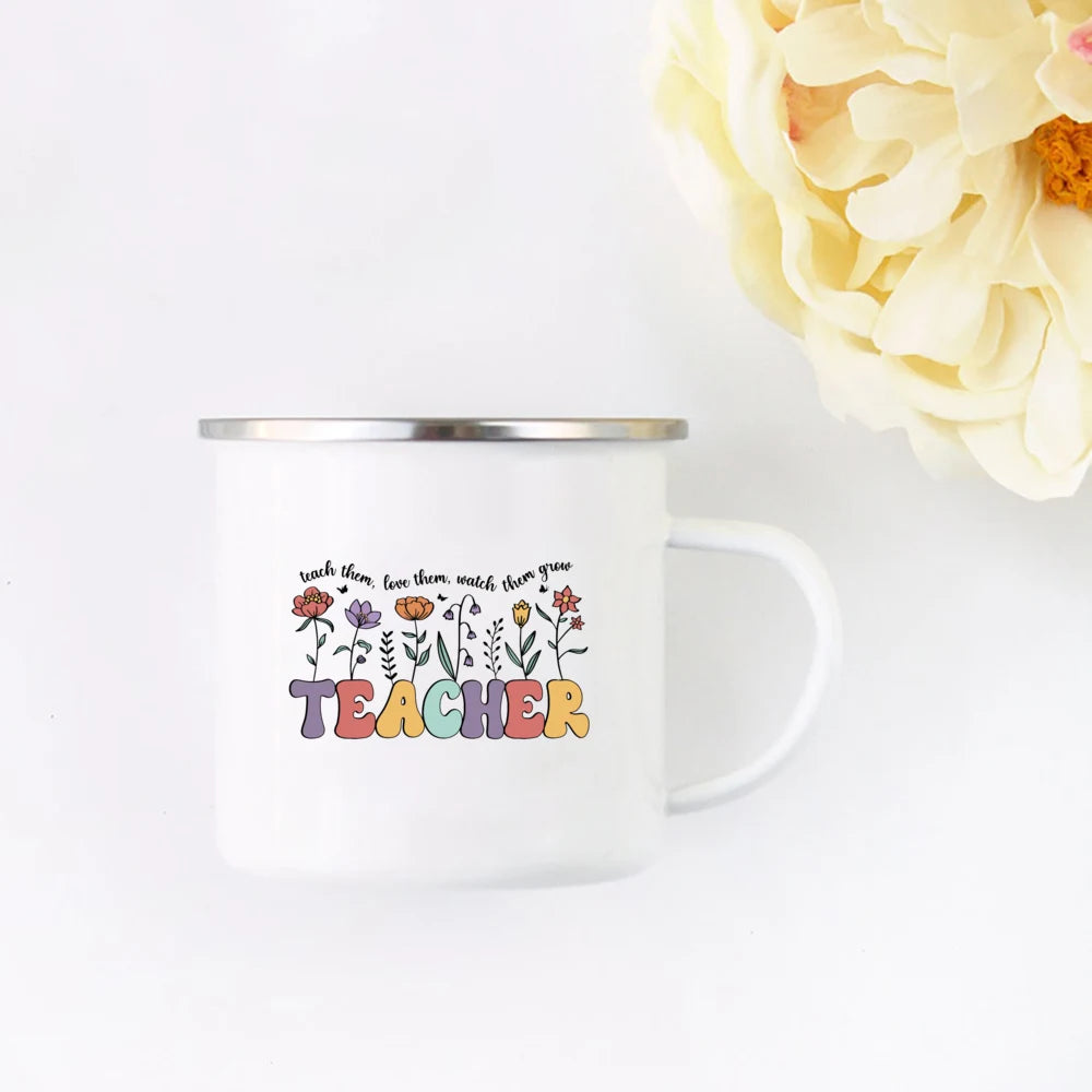 A white enamel mug with a floral design and the word TEACHER printed on it, set against a white background.