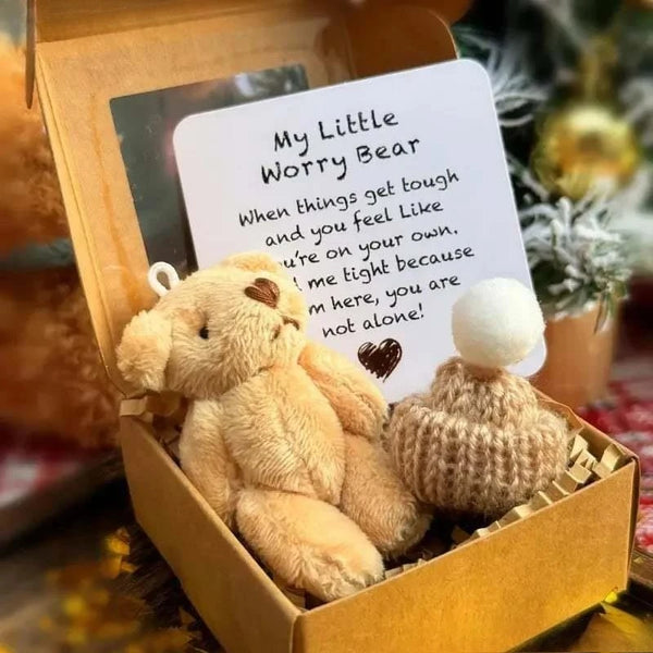 A fluffy light brown worry bear plush toy resting in a gold gift box with an encouraging card.