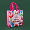 A pink reusable happy birthday gift bag with a decorative lace border and colorful balloons.
