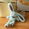 A light blue giant kawaii rabbit plush toy with brown accents sitting on a wooden surface next to a beige bag.