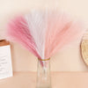 Un ramo de plumas de pampas artificiales rosa y blanco en un jarrón de vidrio transparente.