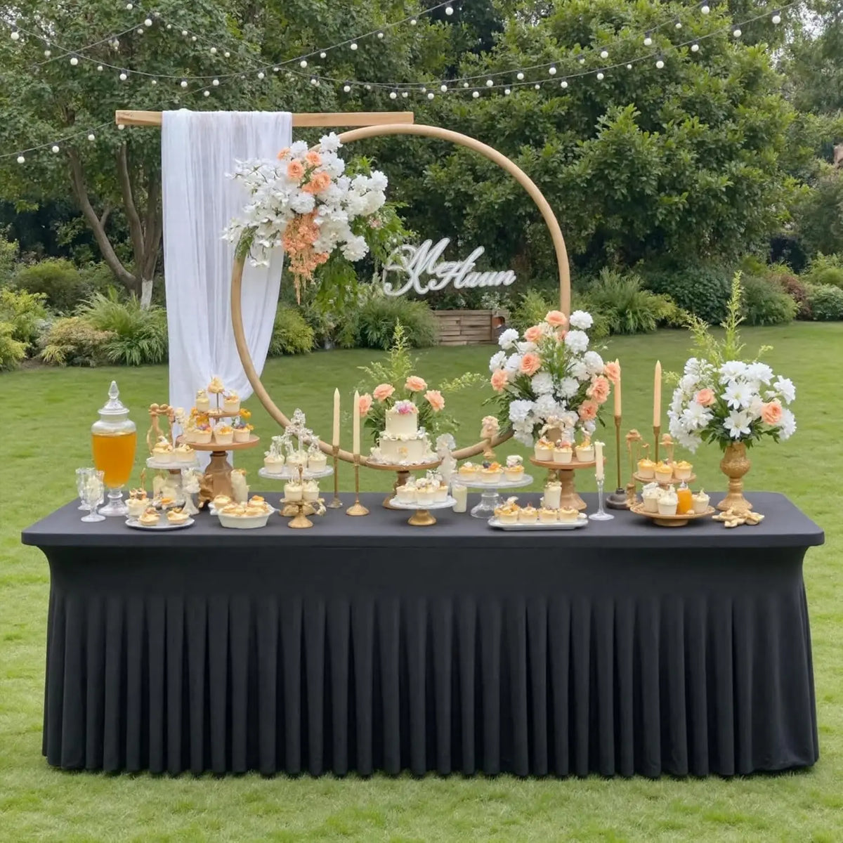A black pleated tablecloth display featuring floral arrangements and a gold hoop backdrop for an event.