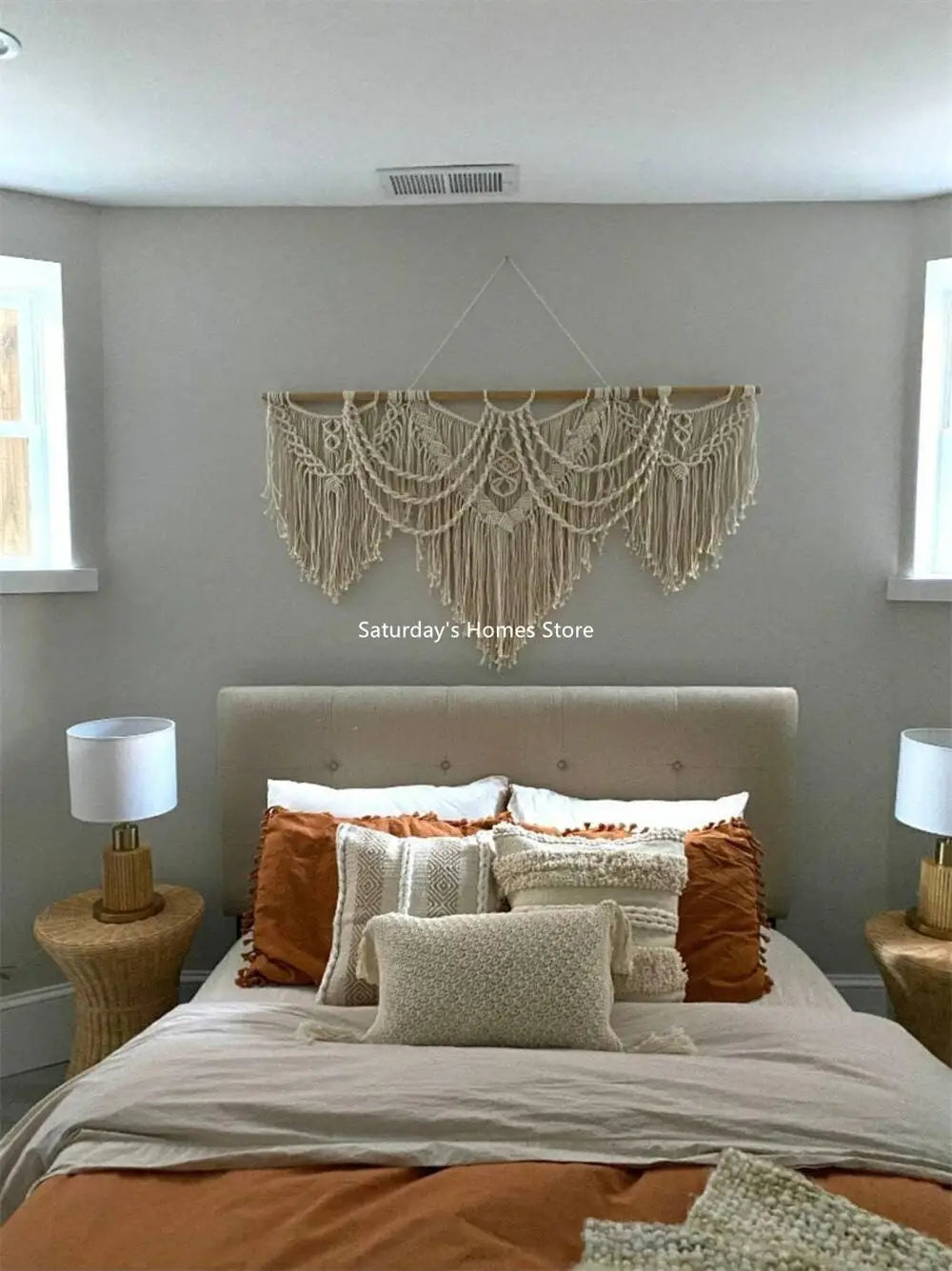 A bedroom featuring a neutral-toned bed with layered pillows and a macrame wall hanging tapestry above the headboard.