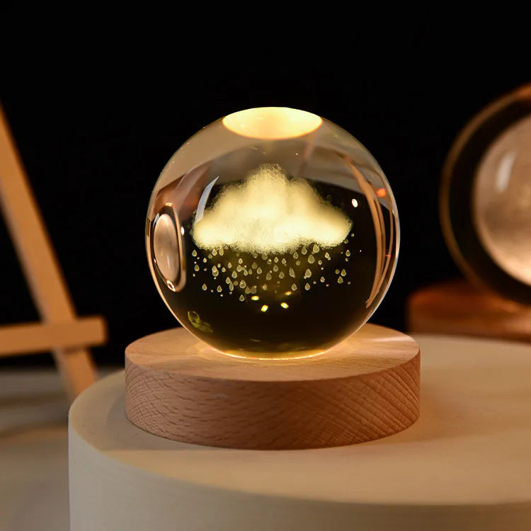 A glass crystal ball night light with a glowing yellow light rests on a round wooden base.