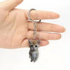 A small gray tabby kitten charm attached to a silver hoop keychain held in a person's hand.