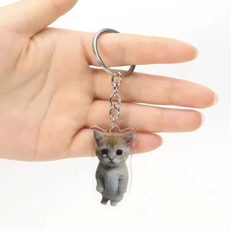 A small gray tabby kitten charm attached to a silver hoop keychain held in a person's hand.