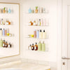 A display of various skincare and beauty products stored in clear acrylic floating racks on a white wall.