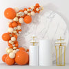 A display of orange and cream latex balloons arranged in a decorative cluster next to white cylindrical containers.