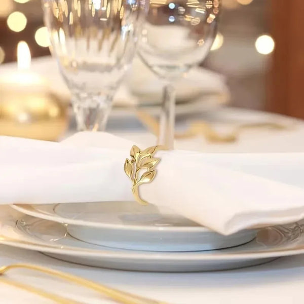 Gold alloy napkin rings decorating a white table setting with glassware and candlelight.