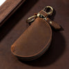 A brown leather key pouch with a metal carabiner attached, resting on a dark brown surface.