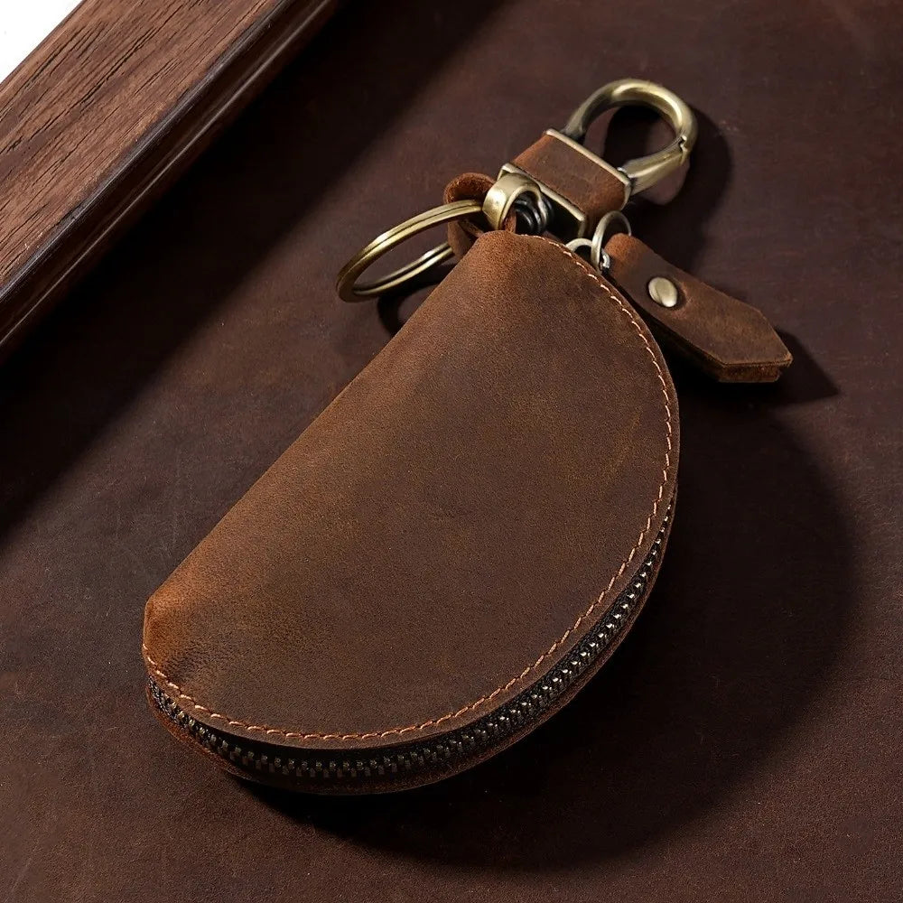A brown leather key pouch with a metal carabiner attached, resting on a dark brown surface.