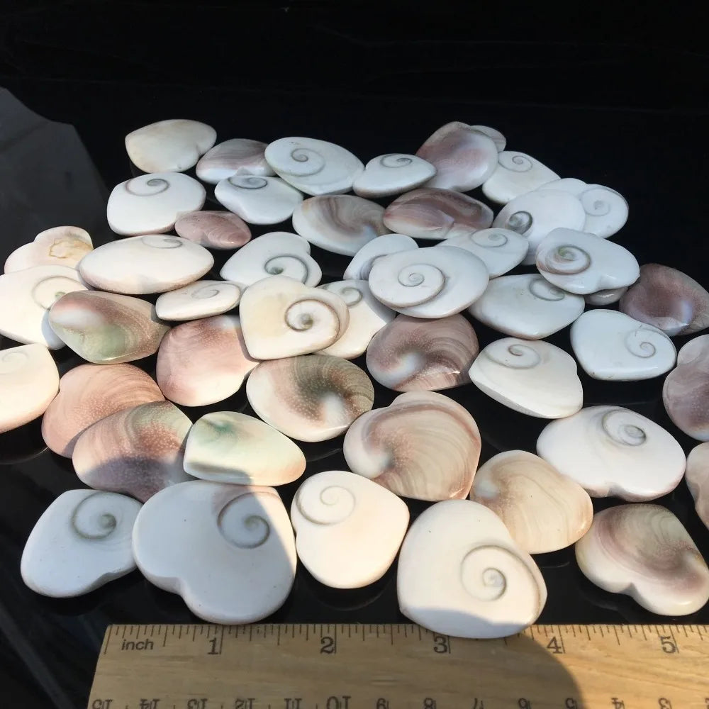 A collection of natural rose quartz heart stones with a Shiva eye for love and protection arranged on a dark surface.