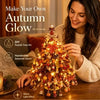 A woman is decorating a DIY Fall Tree Glow kit with warm lights and seasonal decorations.