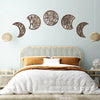 Nordic wooden moon phase wall art featuring various cut-out silhouettes on a light blue wall above a bed.