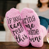 Pair of pink plush slipper socks with black text reading If you can read this bring me some wine