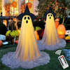 A large, glowing ghost decoration with a black hat and white face is displayed outdoors in a garden setting.