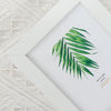 A white photo frame displaying a green palm leaf watercolor illustration on a white background.