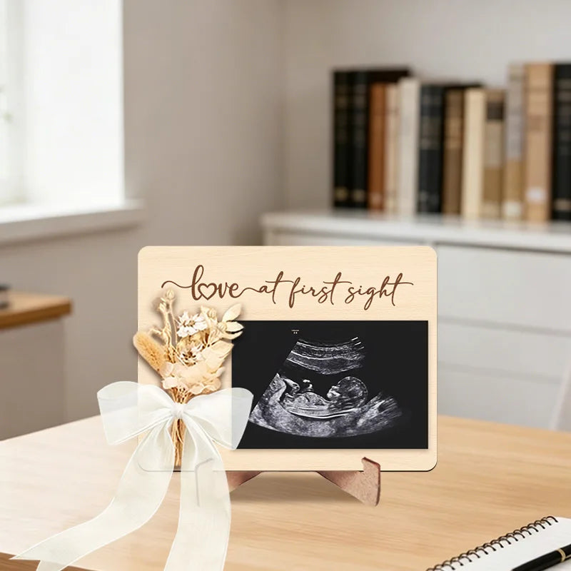 A wooden ultrasound photo frame featuring an ultrasound image and a floral ribbon for a pregnancy announcement.