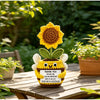 Hand crocheted sunflower bee potted ornament with a yellow flower and fuzzy body sitting on a wooden table.
