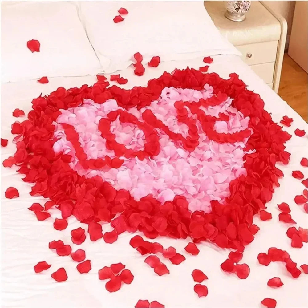 Un cœur fait de pétales de roses artificielles rouges et roses dispersés sur une surface blanche.