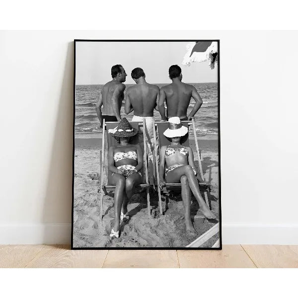 A black and white photograph of four people posing on a beach with a ladder.