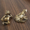Antique brass frog sculpture decor resting on a dark wooden surface.