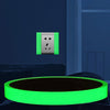 A glowing neon green safety warning tape is placed on a dark surface next to a silver electrical outlet.