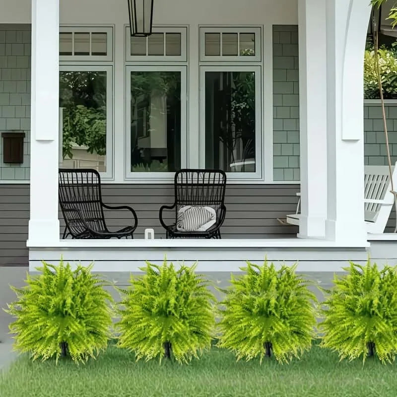 Two artificial green fern stakes planted in a lawn in front of a gray house